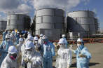Members of the media, wearing protective suits and masks, walk after they receive briefing from Tokyo Electric Power Co. (TEPCO) employees (in blue) in front of storage tanks for radioactive water at TEPCO's tsunami-crippled Fukushima Daiichi nuclear power plant in Okuma town, Fukushima prefecture, Japan February 10, 2016. REUTERS/Toru Hanai - RTX26APO