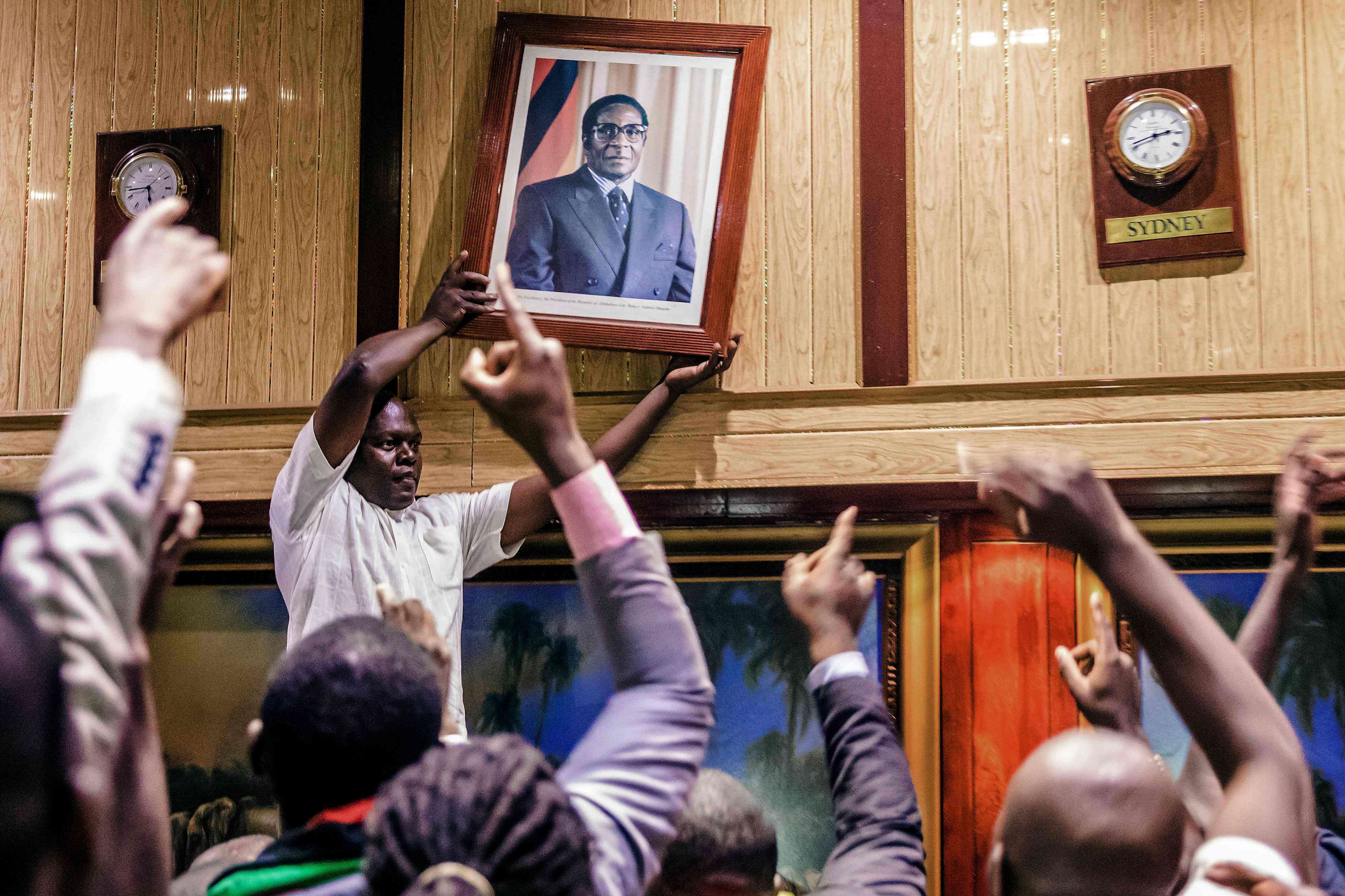 Un homme enlève du mur du Centre de conférence international le portrait de l’ancien président zimbabwéen Robert Mugabe, le 21 novembre, jour de sa démission après trente-sept ans au pouvoir. Le président était assigné à résidence dans sa villa depuis l’intervention de l’armée pour le destituer.