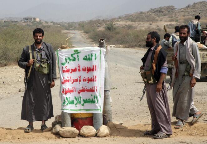 Des insurgés houthistes se tiennent à un point de contrôle à Saada, dans le nord-ouest du Yémen, le 16 février 2010.  Une banderole, en arabe, reprend leur slogan : 
