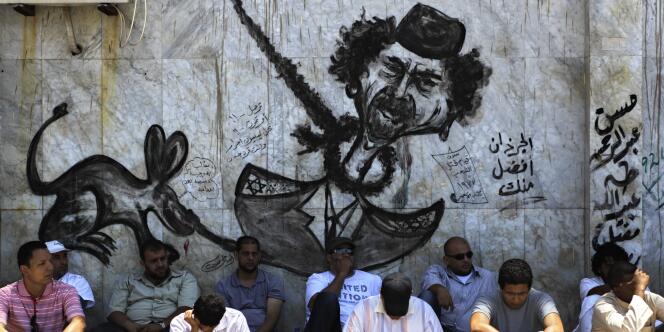 Des Libyens sous un graffiti représentant Kadhafi, avant la prière du vendredi, à Benghazi.