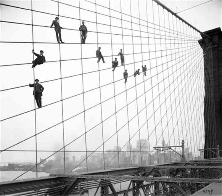 In this Oct. 7, 1914 photo provided by the New York City Municipal Archives, painters are suspended from wires on the Brooklyn Bridge in New York. Over 870,000 photos from an archive that exceeds 2.2 million images have been scanned and made available online, for the first time giving a global audience a view of a rich collection that documents life in New York City. (AP Photo/New York City Municipal Archives, Department of Bridges/Plant & Structures, Eugene de Salignac) MANDATORY CREDIT