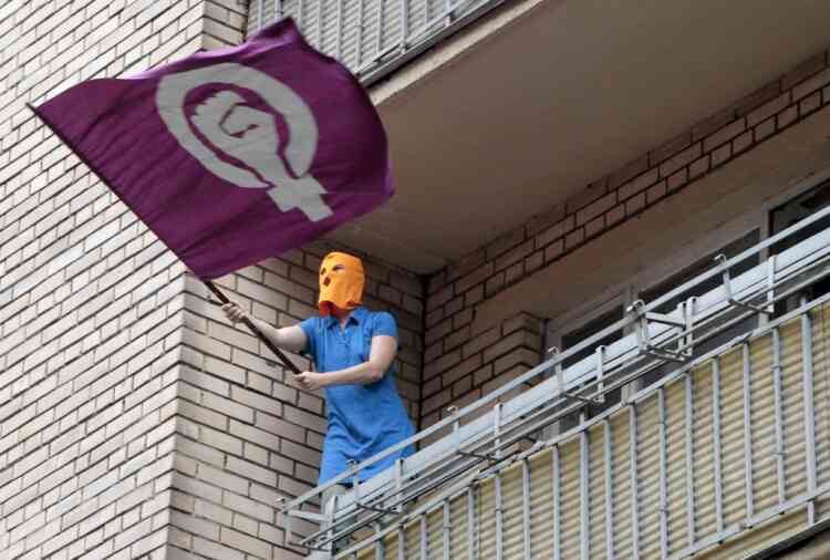 A masked supporter of the Russian punk group Pussy Riot waves a feminist flag from a balcony of a building at the court  in Moscow, Russia, Friday, Aug. 17, 2012. A Moscow judge has sentenced each of three members of the provocative punk band Pussy Riot to two years in prison on hooliganism charges following a trial that has drawn international outrage as an emblem of Russia's intolerance to dissent. (AP Photo/Misha Japaridze)