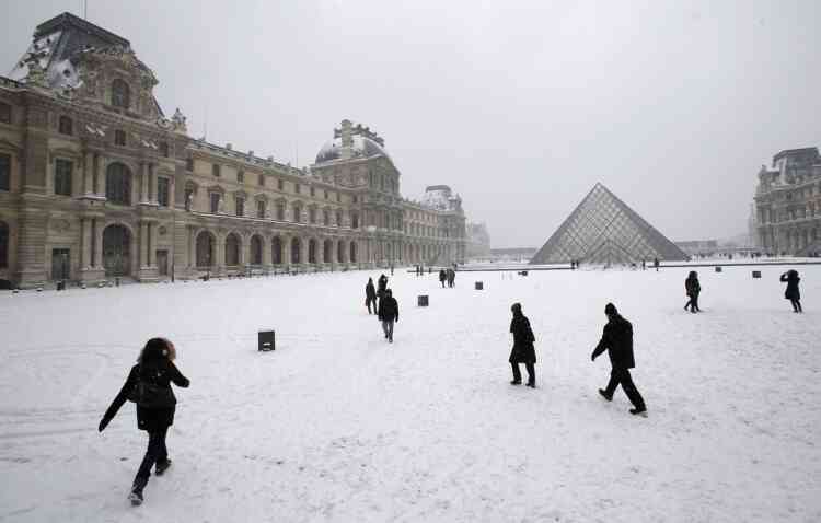 People stroll in the snow covered square of the Louvre museum, after a snowfall in Paris, Sunday, Jan. 20, 2013. (AP Photo/Christophe Ena)