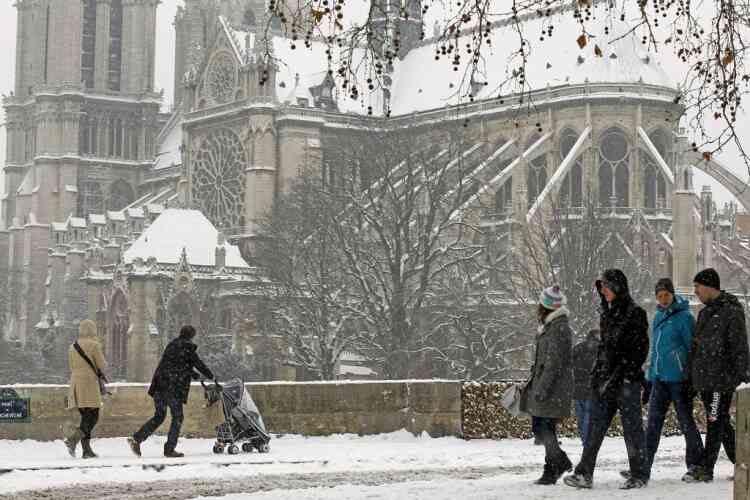 Tourists and Parisians walk behind Notre Dame cathedral during snow fall,  in Paris, Sunday, Jan. 20, 2013. (AP Photo/Remy de la Mauviniere)