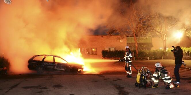 Des pompiers éteignent un véhicule incendié, le 21 mai, à Kista, dans la banlieue de Stockholm.