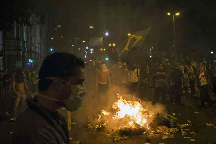 Protesters, one holding a Brazilian flag,  burn trash to block a street near the sate legislative assembly building during a protest in Rio de Janeiro, Brazil, Monday, June 17, 2013.  in Rio de Janeiro, Brazil, Monday, June 17, 2013.  Officers in Rio fired tear gas and rubber bullets when a group of protesters invaded the state legislative assembly and threw rocks and flares at police. Protesters massed in at least seven Brazilian cities Monday for another round of demonstrations voicing disgruntlement about life in the country, raising questions about security during big events like the current Confederations Cup and a papal visit next month.  (AP Photo/Felipe Dana)