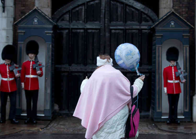 A royal fan holding a christening celebration balloon watches as members of the Grenadier Guards mount guard outside St James's Palace in London, Wednesday, Oct. 23, 2013. Britain's Prince George, son of Prince William and Kate Duchess of Cambridge and who is third in line to the throne will be christened in the Chapel Royal inside the palace Wednesday. (AP Photo/Alastair Grant)
