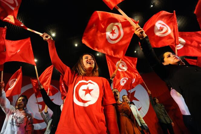 Des Tunisiens brandissent le drapeau national lors du troisième anniversaire de la fuite de l'ancien président Zinedine El-Abidine Ben Ali, le 14 janvier 2014 sur l'avenue Habib-Bourguiba, à Tunis.