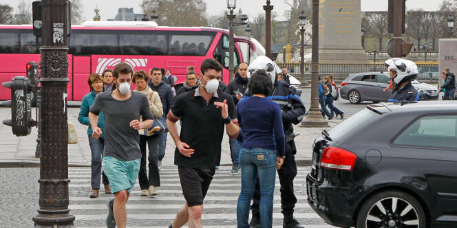Des joggers courent dans une rue de Paris, en essayant de se protéger de la pollution. Au second plan, la police contrôle la circulation, réglementée dans la capitale et dans ses communes limitrophes, le 17 mars