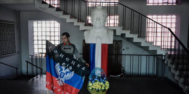 Un militant prorusse tenant dans les mains un drapeau de la République de Donetsk dans le hall de la mairie de la ville de Torez, à côté d'un portrait de Maurice Thorez.