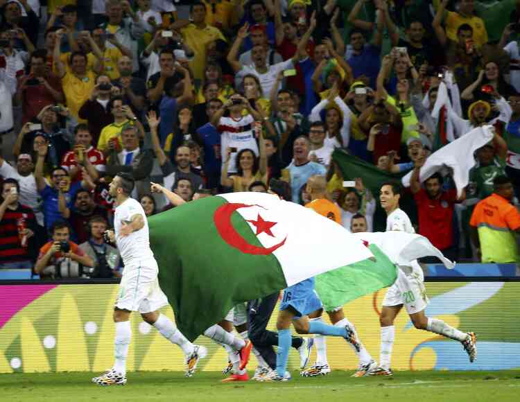 Algeria's players carry their national flag as they celebrate at the end of their 2014 World Cup Group H soccer match against Russia at the Baixada arena in Curitiba June 26, 2014.          REUTERS/Murad Sezer (BRAZIL  - Tags: SOCCER SPORT WORLD CUP)