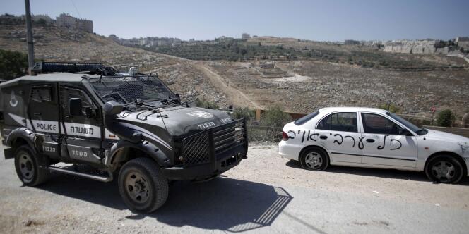 Un véhicule de la police israélienne à proximité d'un véhicule sur lequel a été peint un slogan xénophobe (