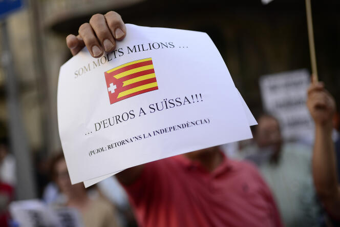 Manifestation à Barcelone, le 30 juillet. Un homme brandit un drapeau catalan détourné avec la légende : « Nous sommes plusieurs millions... d’euros en Suisse !!! (Pujol: nous refusons l’indépendance). »