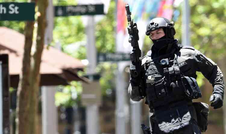 An armed policeman is seen outside a cafe in the central business district of Sydney on December 15, 2014. Hostages were being held inside a cafe in central Sydney on December 15 with an Islamic flag displayed against a window, according to witnesses and reports, while police said they were also responding to an "incident" at the nearby Opera House. AFP PHOTO / SAEED KHAN
