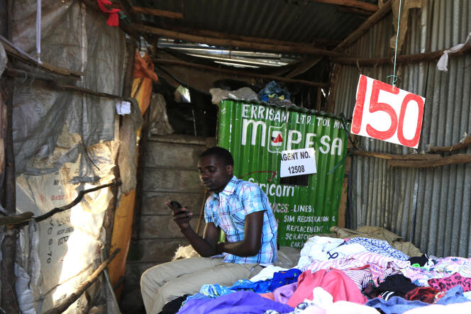 Brian Ochieng attend des clients de M-Pesa dans sa friperie de Kibera, à Nairobi, le 31 décembre 2014.