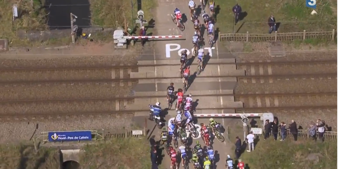 Des coureurs du Paris-Roubaix franchissent un passage à niveau avant le passage d'un TGV