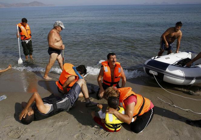 Sur une plage de l'île grecque de Kos, le 15 août 2015. Un touriste passe devant un groupe de migrants iraniens épuisés. Ces derniers viennent tout juste de débarquer de leur petite embarcation non motorisée.