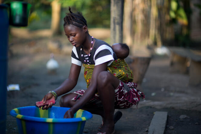 Amina Kamara, 15 ans, fait la lessive avec son fils de six mois sur le dos. Village de Motonko, dans le district de Moyamba, en Sierra Leone, novembre 2015.