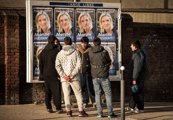 Des migrants à Calais devant un panneau placardé d'affiches du FN le 6 décembre 2015.