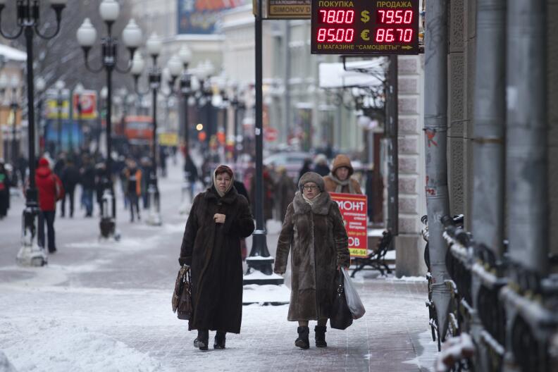 People walk at a street passing an exchange booth in Moscow, Russia, Monday, Jan. 18, 2016. The Russian ruble, battered by weak oil prices, on Monday dropped to new low and broke an all-time record against the euro. (AP Photo/Ivan Sekretarev)