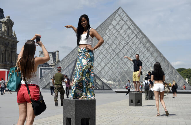 Des touristes se photographient devant la pyramide du Louvre.