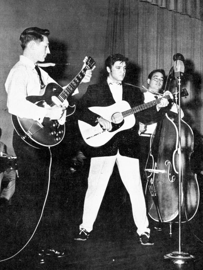 Elvis Presley sur scène en 1957, entouré du guitariste Scotty Moore (gauche) et du contrebassiste Bill Black (droite).