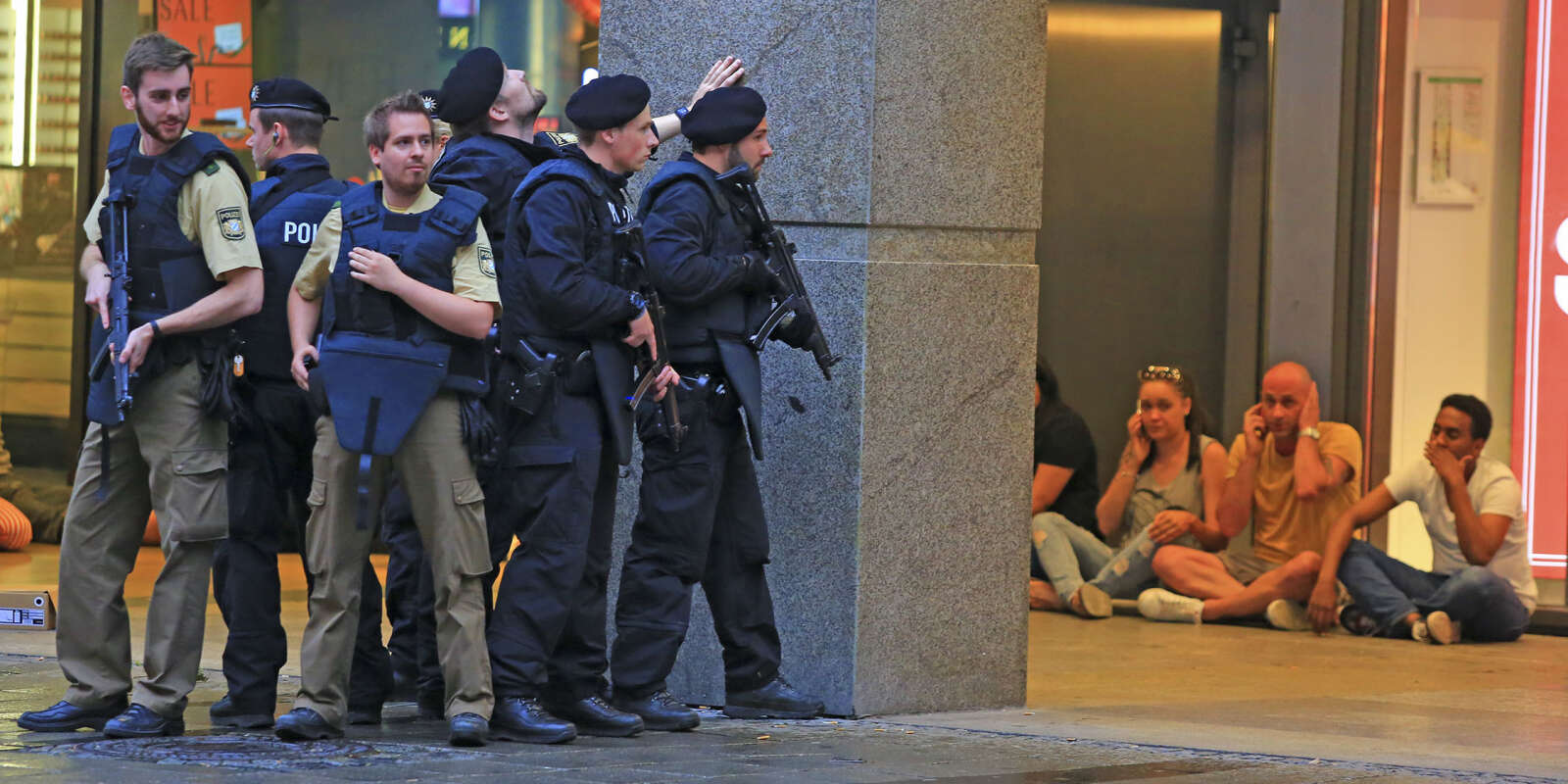 In this Friday, July 22, 2016 photo provided by Wael Ladki people take shelter as armed police officers are on the hunt for possible fugitives after a shooting in a shopping mall in Munich, southern Germany. A gunman killed 9 people before killing himself. (Wael Ladki via AP)