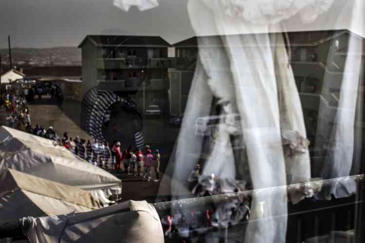 Une femme et un enfant sont aperçus dans le reflet d’une vitre surplombant une file de votants à KwaMashu au nord de Durban.