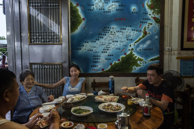 Une famille de touristes chinois, en visite sur l'ile de Hainan, dîne  dans un restaurant de fruits de mer. Sur le mur, une carte montre les revendications maritimes chinoises et les récifs disputés.