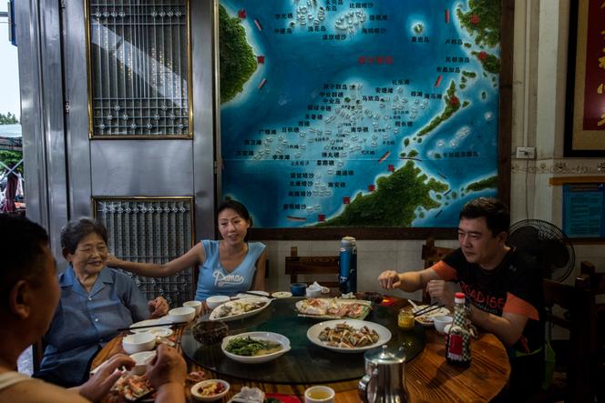 Une famille de touristes chinois, en visite sur l'ile de Hainan, dîne  dans un restaurant de fruits de mer. Sur le mur, une carte montre les revendications maritimes chinoises et les récifs disputés.