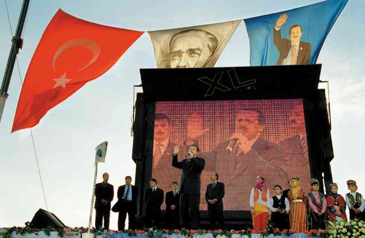 Sur cette photo prise à Istanbul en octobre 2002, Recep Tayyip Erdogan, leader du Parti  de la justice et du développement (AKP) qu’il a fondé un an plus tôt, est en campagne. Il deviendra premier ministre quelques mois plus tard. Au-dessus de l’estrade, entre son portrait et le drapeau turc, flotte au vent la figure de Mustafa Kemal Atatürk, fondateur de la Turquie moderne, dont il fut le premier président de la Républiquede 1923 à 1938. Quinze ans après ce cliché, Erdogan, devenu président à son tour, s’apprête, s’il remporte le référendum du 16 avril, à modifier la Constitution. Ses opposants, qui dénoncent depuis longtemps son entreprise de déconstruction de la République laïque fondée par Atatürk, s’inquiètent cette fois-ci d’une révision constitutionnelle, qui prévoit le renforcement du pouvoir présidentiel en supprimant notamment le poste de premier ministre.