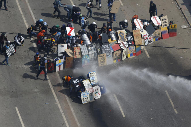 Des manifestants se protègent des canons à eau de la police anti-émeutes avec leurs pancartes, lundi 29 mai 2017 à Caracas, lors d’une manifestation contre le régime du président vénézuélien, Nicolas Maduro.