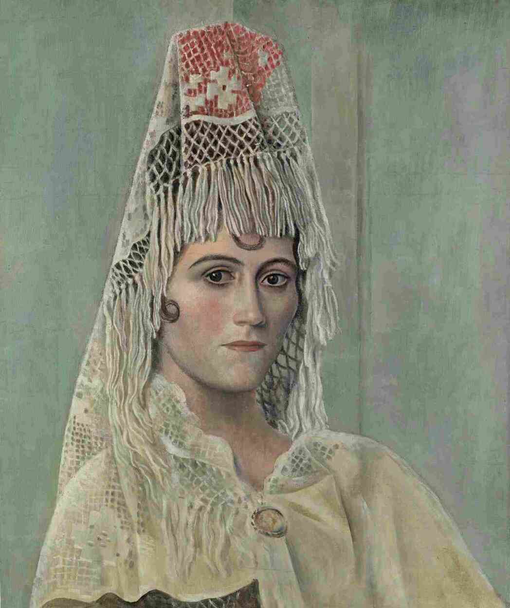 « “Olga à la mantille” est l’un des tout premiers portraits d’Olga, que Picasso a rencontrée lors de son séjour à Rome en 1917. L’artiste la dépeint avec naturalisme et distance, en la dotant significativement d’une coiffe catalane, accessoire typique du costume traditionnel espagnol, improvisé à partir d’un napperon de guéridon. »
