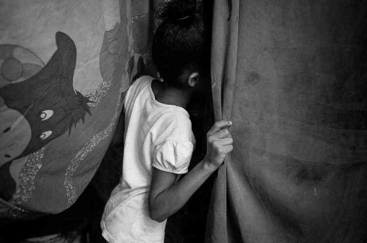 Une petite fille passe une tête entre les draps faisant office de porte de sa maison, dans le quartier de Petare à Caracas.