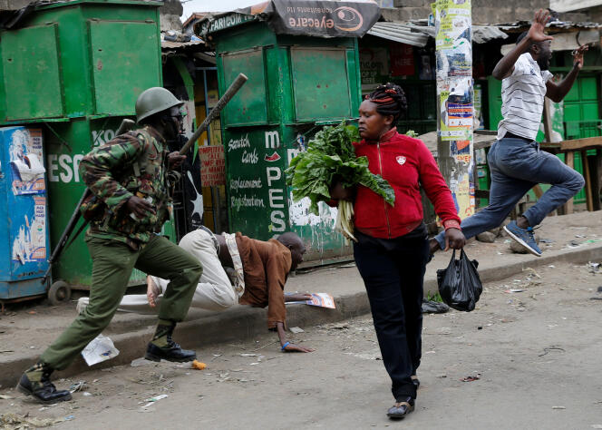 Un policier anti-émeute essaie de disperser des manifestants pendant qu’une femme continue son marché à Mathare, à Nairobi, le 9 août.