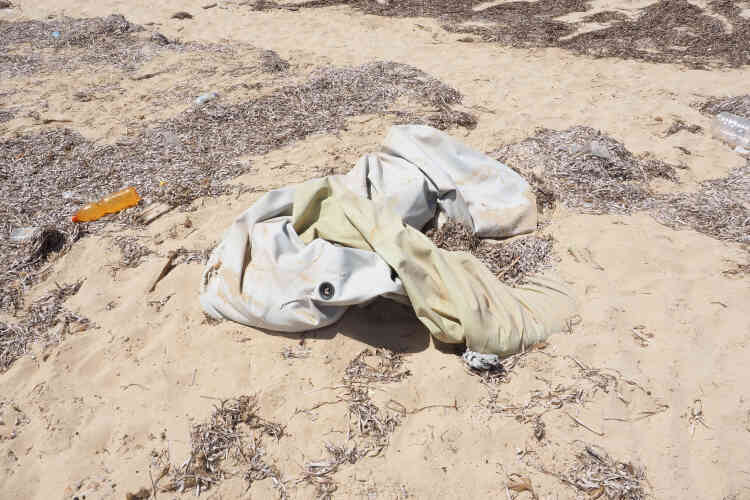 Sur la plage à coté du site archéologique de la ville de Sabratha, un Zodiac blanc est enfoui dans le sable. Ce type de Zodiac est celui utilisé par les migrants pour faire la traversée. Au dessus se trouvent un tas d’habits, des déchets et quelques bidons d’eau.