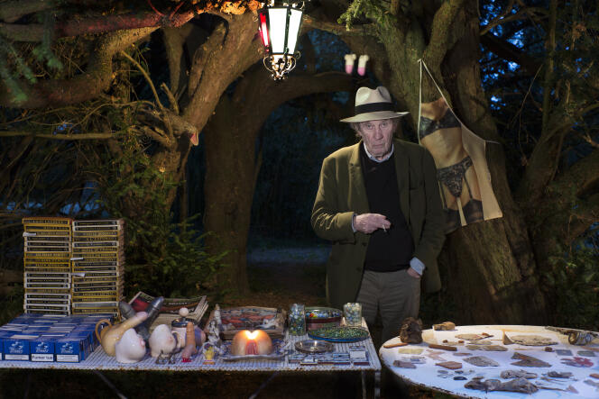 André S. Labarthe dans le jardin de sa maison de campagne des Deux-Sèvres, le 3 août. Il présente, tel un brocanteur du soir, ses collections d’objets érotiques, de billes, de polars et d’objets écrasés. Au premier plan de la table ronde, un rat mort.