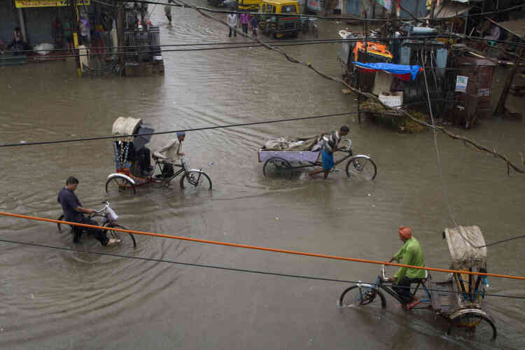Des tireurs de pousse-pousse indiens traversent un carrefour inondé après de fortes pluies, à Allahabad.