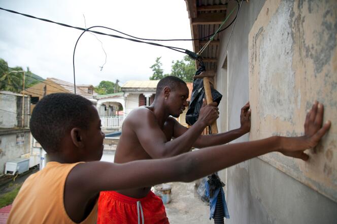 Deux jeunes hommes accrochent des planches en bois sur les fenêtres à Trois-Rivières en Guadeloupe.