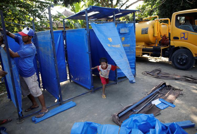 Un garçon joue dans les douches mobiles du camps à Manggis.