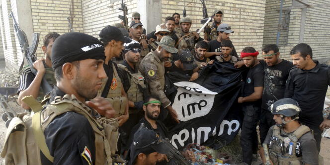 Des soldats irakiens posent avec un drapeau de l’Etat islamique pris aux terroristes à l’universitré d’Anbar, en juillet 2015.