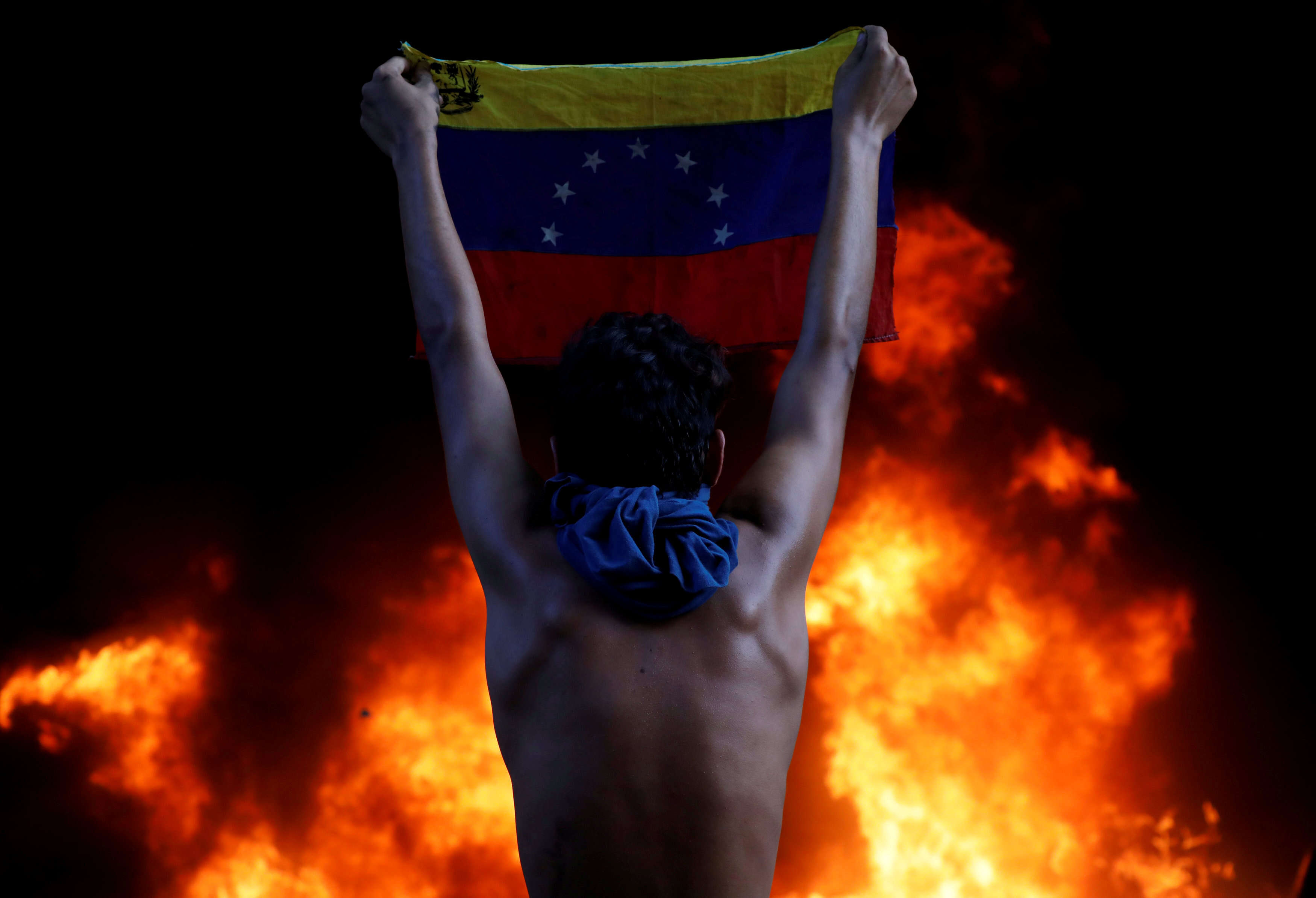 Un manifestant brandit un drapeau vénézuelien devant un feu, à l’entrée d’un immeuble abritant la magistrature de la Cour suprême de justice et une succursale bancaire, lors d’un rassemblement contre le président du Venezuela, Nicolas Maduro. Depuis son arrivée au pouvoir, en 2013, après la mort de Hugo Chavez, le pays s’est enfoncé dans une grave crise économique, politique et sociale. Depuis plusieurs mois , les contestations ont entraîné des centaines de blessés et de morts.