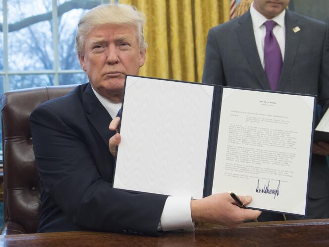 Le président américain Donald Trump brandit le décret mettant fin à la participation des Etats-Unis au traité de libre-échange transpacifique (TPP), le 23 janvier 2017 dans le bureau Ovale de la Maison Blanche à Washington.