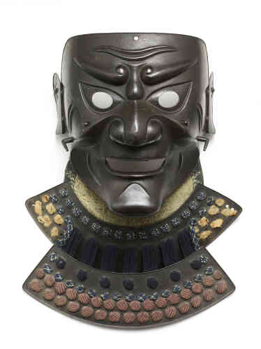 « Ce masque de protection faciale eut d’abord pour fonction de compléter le casque pour couvrir le visage et effrayer l’ennemi. A l’époque d’Edo (1603-1868), de tels masques servaient non plus pour les combats mais pour la parade ou pour être exposés, donnant une présence plus forte et terrifiante à l’armure du guerrier. »