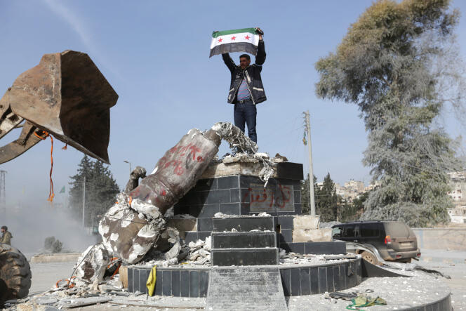 Un combattant de l’Armée syrienne libre brandissant le drapeau de sa faction devant une statue kurde renversée.