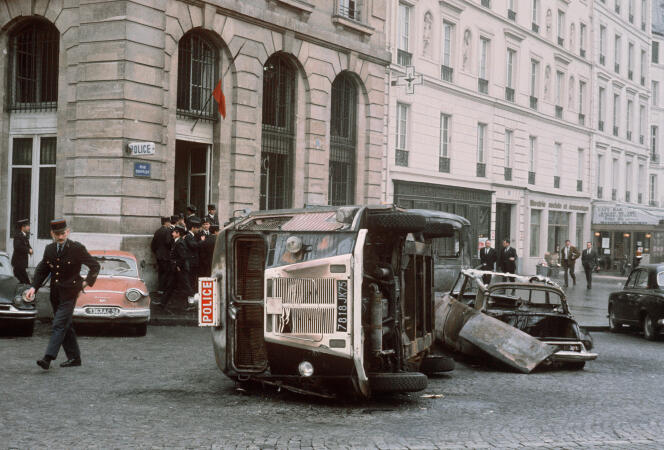 Un policier inspecte le 25 mai 1968 une voiture de police renversée et une autre incendiée lors des échauffourées qui ont opposé des étudiants aux forces de l’ordre dans la nuit, au quartier Latin à Paris.