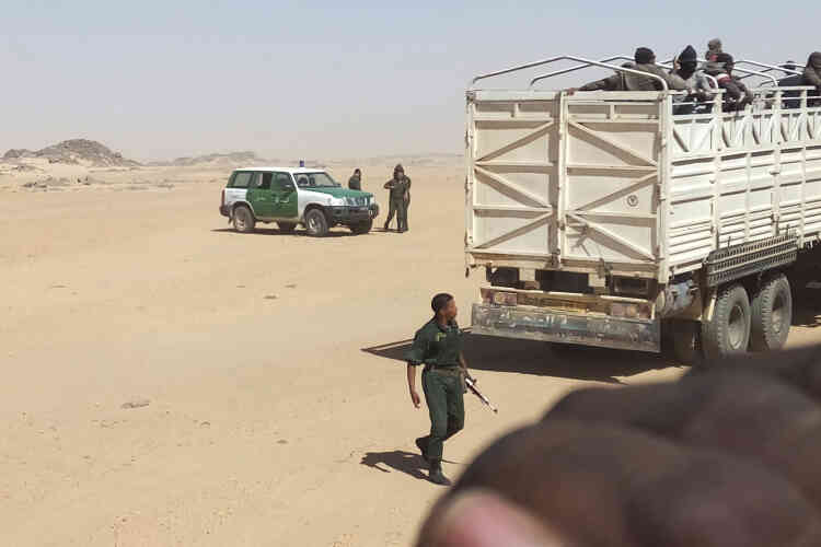 Des gendarmes algériens armés font monter des migrants dans des camions pour les déposer à la frontière du Niger.