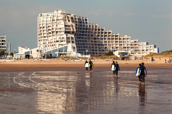 A Saint-Jean-de-Monts, des surfeurs marchent sur la plage devant l’immeuble Arc-en-ciel.