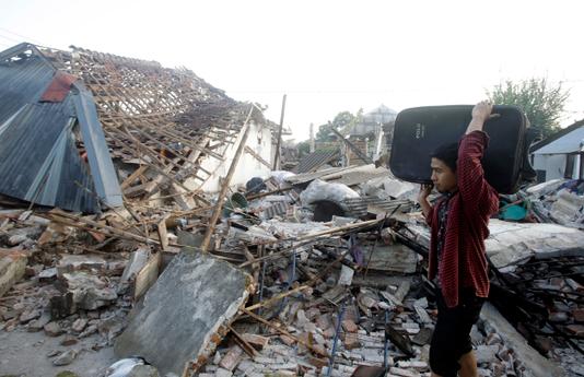 Un homme transporte quelques affaires au milieu des maisons en ruine dans un village, sur l’île de Lombok en Indonésie, le 9 août.