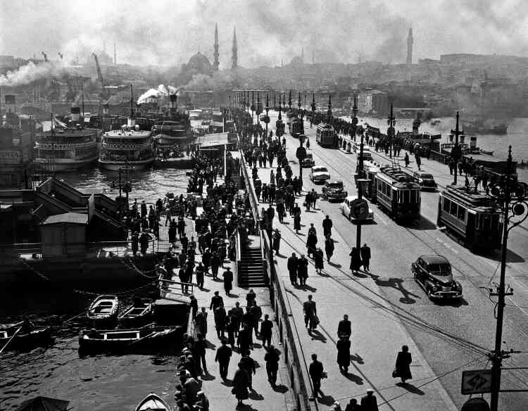 Des passants sur le vieux pont de Galata. Avec cette photographie célèbre, Ara Güler met en évidence la superposition des périodes historiques que rend possible Istanbul. Cette idée qui lui était chère est traduite par les trajectoires parallèles et séparées de passants en costume et chapeau et de travailleurs de la rue en pantalon bouffant et béret.